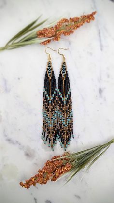 two pairs of beaded earrings sitting on top of a marble counter next to plants