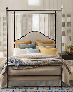 a four poster bed with pillows and blankets on it in a white room next to a window