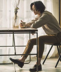 a person sitting at a table with a coffee cup in their hand and looking down