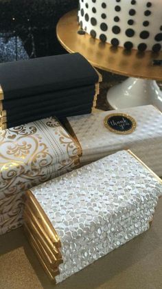 a table topped with lots of cake covered in gold and black wrappings on top of each other