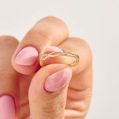 a woman's hand with pink and gold nail polish holding a ring on her finger