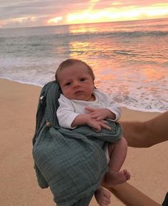 a woman holding a baby on the beach at sunset with waves crashing in front of her