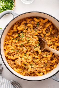 a pot filled with pasta and meat on top of a white table next to some parsley