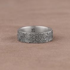 a silver ring with an intricate design on the outside and inside, sitting on a brown surface