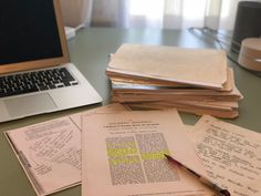 a laptop computer sitting on top of a desk next to stacks of papers and pens