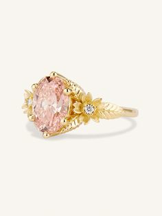 an oval pink diamond ring with leaves on the band and two small white diamonds around it