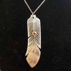 a silver and gold feather pendant on a black surface with a chain attached to it