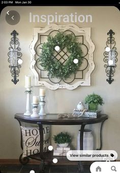 a console table with wreaths and candles on it in front of a wall hanging