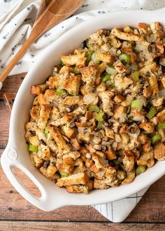 a casserole dish with stuffing in it on a wooden table next to utensils