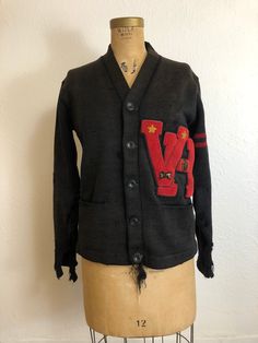 "Vintage 1950's letterman cardigan sweater. Nicely worn and faded. Buttons down the front. Two hip pockets. Double red stripe on one sleeve. \"VH\" red patch. Both sleeves are pretty holey and need repair. There are a few holes on the front, underarm, and back. There is also some unraveling on the front underneath the bottom button. This sweater has a lot of character and is being sold as is. . M E A S U R E M E N T S. measured laying flat, please multiply by two Shoulder to shoulder: 17 inches Black Retro Cotton Cardigan, Vintage Sweater With Pockets For Fall, Vintage Fall Sweater With Pockets, Vintage Crew Neck Cotton Cardigan, Red Vintage Crew Neck Outerwear, Vintage College Sweater For Fall, Vintage College Sweater For Winter, Vintage Sweater For College In Fall, Vintage Sweater For College In Winter