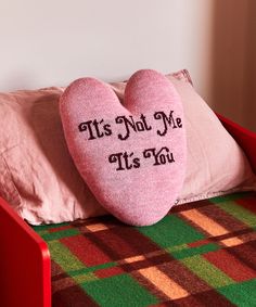 a pink heart shaped pillow sitting on top of a red chair next to a plaid blanket