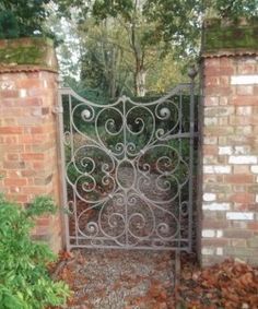 an iron gate in the middle of a brick wall with trees and bushes behind it