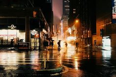 people are walking down the street in the rain at night with umbrellas and lights on