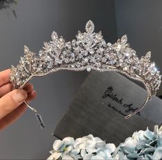 a woman is holding up a tiara with flowers in the foreground and a box behind her