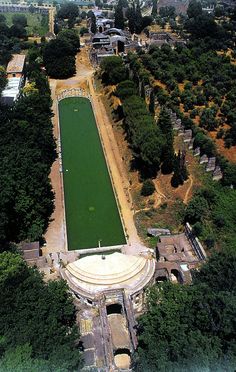 an aerial view of a tennis court surrounded by trees and buildings in the distance,