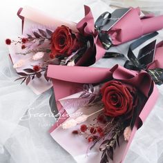 two bouquets of red roses are wrapped in pink paper and tied with black ribbon