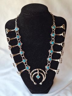 This is a vintage-inspired replica featuring a faux turquoise cabochon squash blossom necklace in silver-tone with a 23" chain. The necklace is substantial, crafted from a metal alloy, and showcases intricate details in the silver-tone finish. It mimics the design of a vintage 1970s Southwestern native silver turquoise necklace. This 1970s reproduction costume piece includes silver metal and faux turquoise in the squash blossom design. It is preowned but in very good condition, with no chips or Western Metal Jewelry Nickel Free, Western Style Silver Necklace For Festivals, Western Style Nickel Free Turquoise Jewelry, Southwestern Silver Turquoise Necklace For Festival, Western Silver Metal Jewelry, Vintage Turquoise Jewelry For Festivals, Vintage Turquoise Necklace For Festivals, Western Silver Turquoise Necklace Nickel Free, Southwestern Silver Turquoise Necklace For Western Events