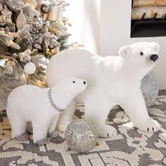 two white polar bears standing next to a christmas tree with silver balls on the floor