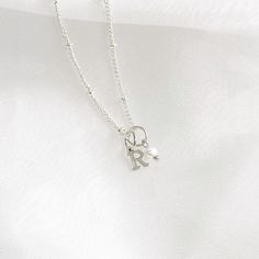 This stunning dainty letter necklace with pearl charm is perfect for anyone looking for understated elegance. The necklace features a delicate silver chain that holds a small, exquisite pearl charm and a capital letter of your choice.  ♡ Handcrafted in our Sydney Studio ♡ Natural Freshwater Pearl ♡ 925 Sterling Silver Plated ♡ Water Resistant ♡ 5mm Charm  PACKAGING: All of our items are carefully packed into a white jewellery box topped with a delicate white satin bow. Our shipping bags are beig Sterling Silver Initial Pendant Charm Necklace With Delicate Chain, Silver Minimalist Initial Necklace With Delicate Chain, Sterling Silver Initial Pendant Necklace With Delicate Chain, Classic Silver Initial Necklace With Delicate Chain, Sterling Silver Initial Necklace With Delicate Chain, Silver Necklace With Pearl Charm For Her, Silver Necklace With Pearl Charm As Gift For Her, Silver Minimalist Initials Name Necklace, Dainty Sterling Silver Initial Necklace For Everyday