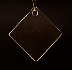 a black square shaped ornament hanging from a gold string on a black background