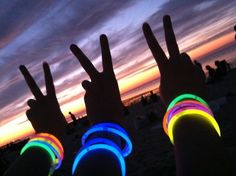 four people with their hands up in the air at sunset or dawn, making peace signs