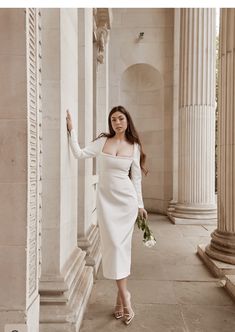 a woman in a white dress is leaning against columns