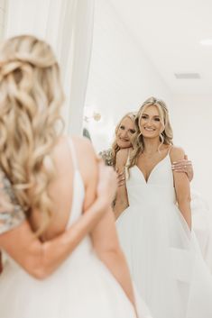 two women in white dresses are looking at their reflection in the mirror while another woman is taking her picture