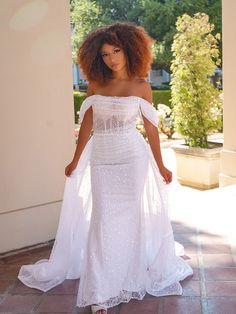 a woman in a white dress standing on a brick walkway with her arms behind her back