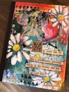 an art journal with flowers and words written on the pages, sitting on a wooden table