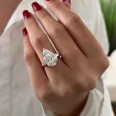 a woman's hand holding a ring with a pear shaped diamond in the middle