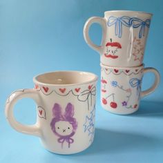 two coffee mugs with designs on them sitting next to each other in front of a blue background