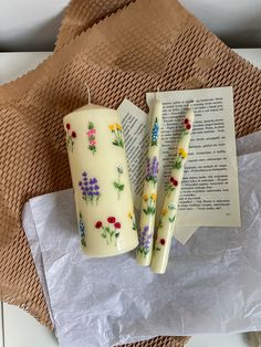 two candles sitting on top of a piece of wax paper next to an open book