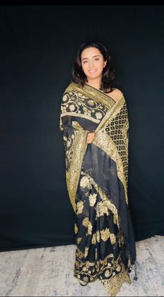 Indulge in timeless elegance with our exquisite Black Banarasi Khaddi Georgette Saree, adorned with lustrous gold zari. This masterpiece seamlessly blends traditional artistry with contemporary sophistication. Crafted from the finest Khaddi Georgette, the saree drapes effortlessly, creating a graceful and ethereal silhouette. The classic black hue serves as the perfect canvas for the intricate gold zari work, which adds a touch of opulence and glamour. Handwoven by skilled artisans, this saree showcases the rich heritage of Banaras. The delicate interplay of light and shadow created by the gold zari on the black base results in a mesmerizing visual effect. Perfect for evening soirees, weddings, or any special occasion where you desire to make a lasting impression. Fabric: Pure Khaddi Georg Black Banarasi Saree, Khaddi Georgette Saree, Saree Drapes, Banarasi Saree, Zari Work, Georgette Saree, Banarasi Sarees, Georgette Sarees, Blouse Dress