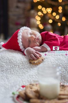 a baby sleeping on top of a white blanket next to a plate of cookies and milk