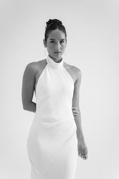 a black and white photo of a woman wearing a dress with high neck, standing in front of a plain background