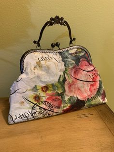 a purse with flowers on it sitting on top of a wooden table next to a wall