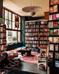 a living room filled with lots of books on top of a book shelf next to a window