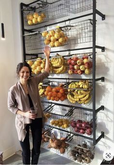 a woman standing in front of a rack full of fruit and vegetables with her hand up