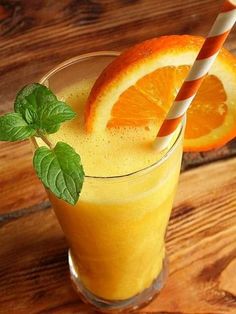 an orange drink is garnished with mint and sliced oranges on a wooden table