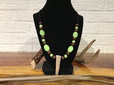 a necklace with green beads is sitting on a stand next to an antelope