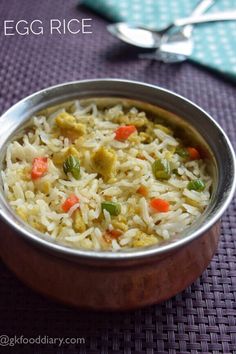 a bowl filled with rice and vegetables on top of a purple table cloth next to spoons