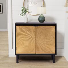 a black and gold cabinet with a mirror above it on the wall next to a plant