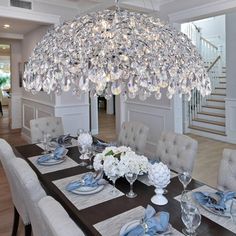 a chandelier hanging from the ceiling over a dining room table with place settings on it