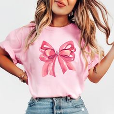 Embrace elegance and flirtatious charm with our captivating pink bow shirt, a delightful addition to your coquette-inspired wardrobe! 🌸👚 This shirt embodies the essence of femininity and playfulness, perfect for those who adore a touch of chic sophistication with a hint of flirtation. 🌷 The darling pink hue complements the shirt's design, accentuating the focal point--an exquisitely crafted oversized bow adorning the neckline or sleeves, adding a whimsical and flirtatious allure to your ensem Cute Bow T-shirt For Spring, Feminine Pink Crew Neck T-shirt, Feminine Party Tops With Bow Detail, Feminine Pink Summer Shirt, Feminine Pink Shirt For Summer, Feminine Tops With Ribbon For Spring, Feminine Ribbon Tops For Spring, Cute Pink T-shirt With Bow, Pink Party Top With Bow