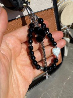 a hand holding a rosary with a heart on it and a cross hanging from the end