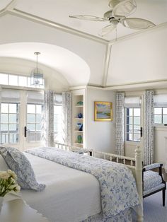 a bedroom with blue and white bedding, windows, and a ceiling fan in the corner