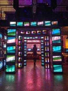 a woman is standing in front of an array of televisions that are lit up