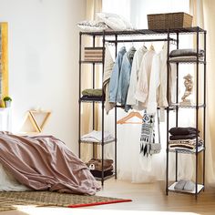 a bedroom with clothes hanging on racks and a bed in the foreground, next to a window