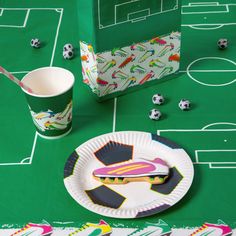 a paper plate with a piece of cake on it next to a cup and soccer field