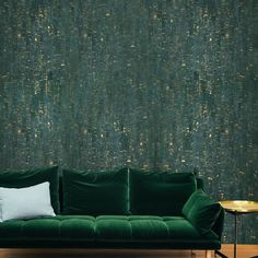 a green couch with two pillows on it in front of a wallpapered background